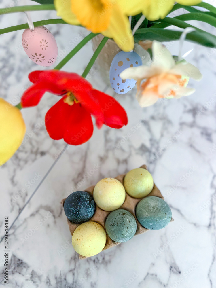 An Easter card. Colorful bright tulips decorated with eggs are in a vase on the table next to colorful eggs. Vertical photography