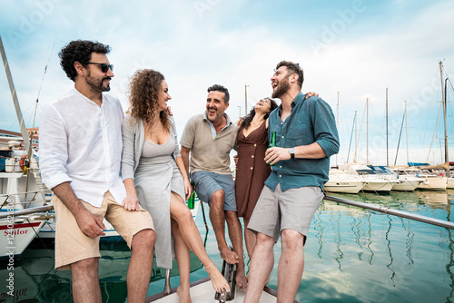Group of friends laughing and enjoying a yacht trip at the marina - summer fun and travel vacation concept
