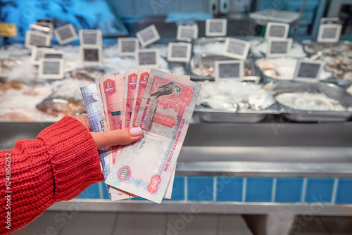 Woman holding United Arab Emirates Dirham banknotes at the fish market