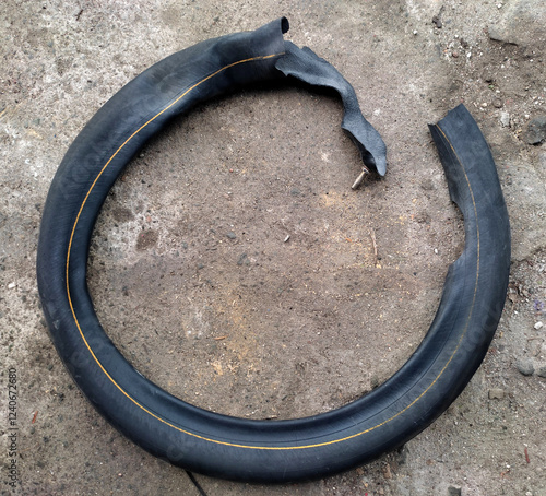 A torn motorcycle inner tube lying on the ground, damaged due to continuous use despite a puncture. The rubber is ripped, exposing layers, with a visible valve stem still attached.