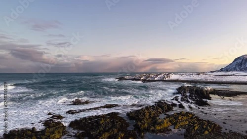 Wallpaper Mural Aerial drone gliding and flying over black rock, sand and snow covered shoreline in a beach at Norway during winter time with mountains in the background during sunset or sunrise with sky orange color Torontodigital.ca