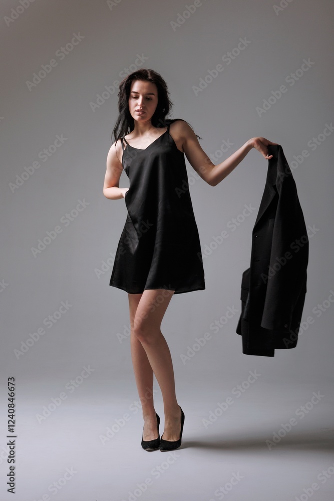 Young woman poses confidently in stylish black dress with jacket in modern studio setting Young woman poses confidently in stylish black dress with jacket in modern studio setting