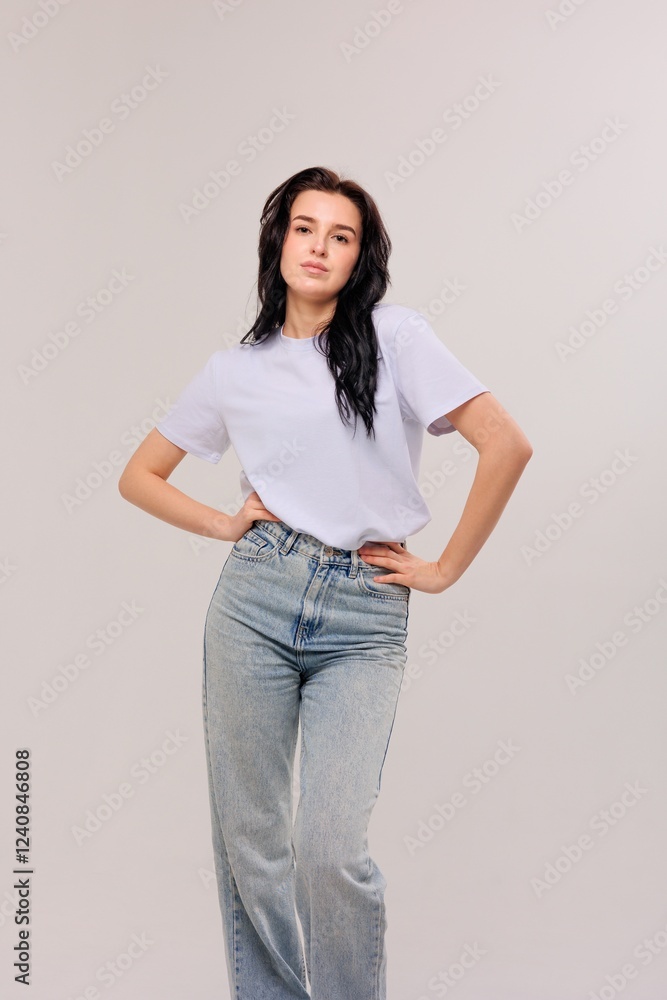 Young woman poses confidently in casual outfit against neutral background during studio photoshoot Young woman poses confidently in casual outfit against neutral background during studio photoshoot