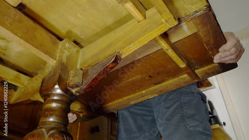 Closeup POV shot from the underneath of a mid 20th century extending oak dining table, with a man’s hands gripping an extra leaf and pulling it out. photo