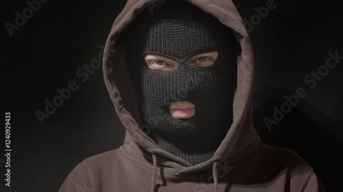 Face covered with balaclava, mask. Portrait of criminal, hacker, anonymous man in hoodie on black background.