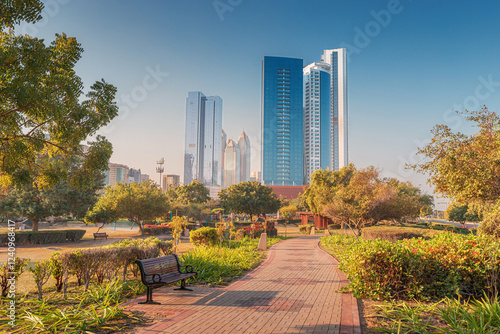 Obraz na płótnie Empty park with bench and brick path leading to modern skyscrapers in Abu Dhabi during sunny morning w salonie