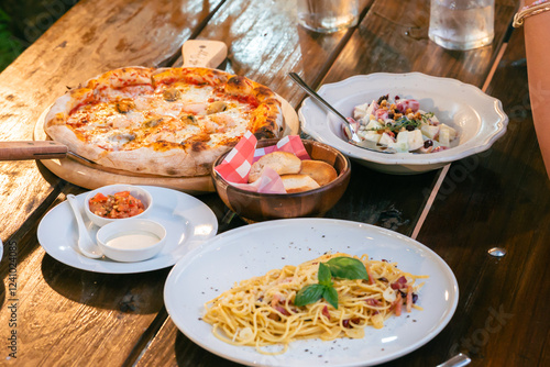  food  from Casa Della Pizza, in Kanchanaburi. The table is set with a delectable spread featuring a crispy, golden pizza topped with fresh a plate of perfectly spaghetti and bowl of  fruit salad