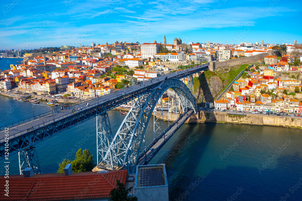 Obraz premium The Dom Luis I Bridge spans the Douro River in Porto, Portugal, connecting historic cityscape with Vila Nova de Gaia. Stunning blend of iron architecture and colorful riverside houses under a blue sky