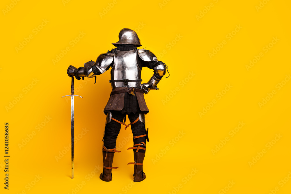 Rear view of a knight in full suit of armor holding a sword against a vivid yellow backdrop Rear view of a knight in full suit of armor holding a sword against a vivid yellow backdrop