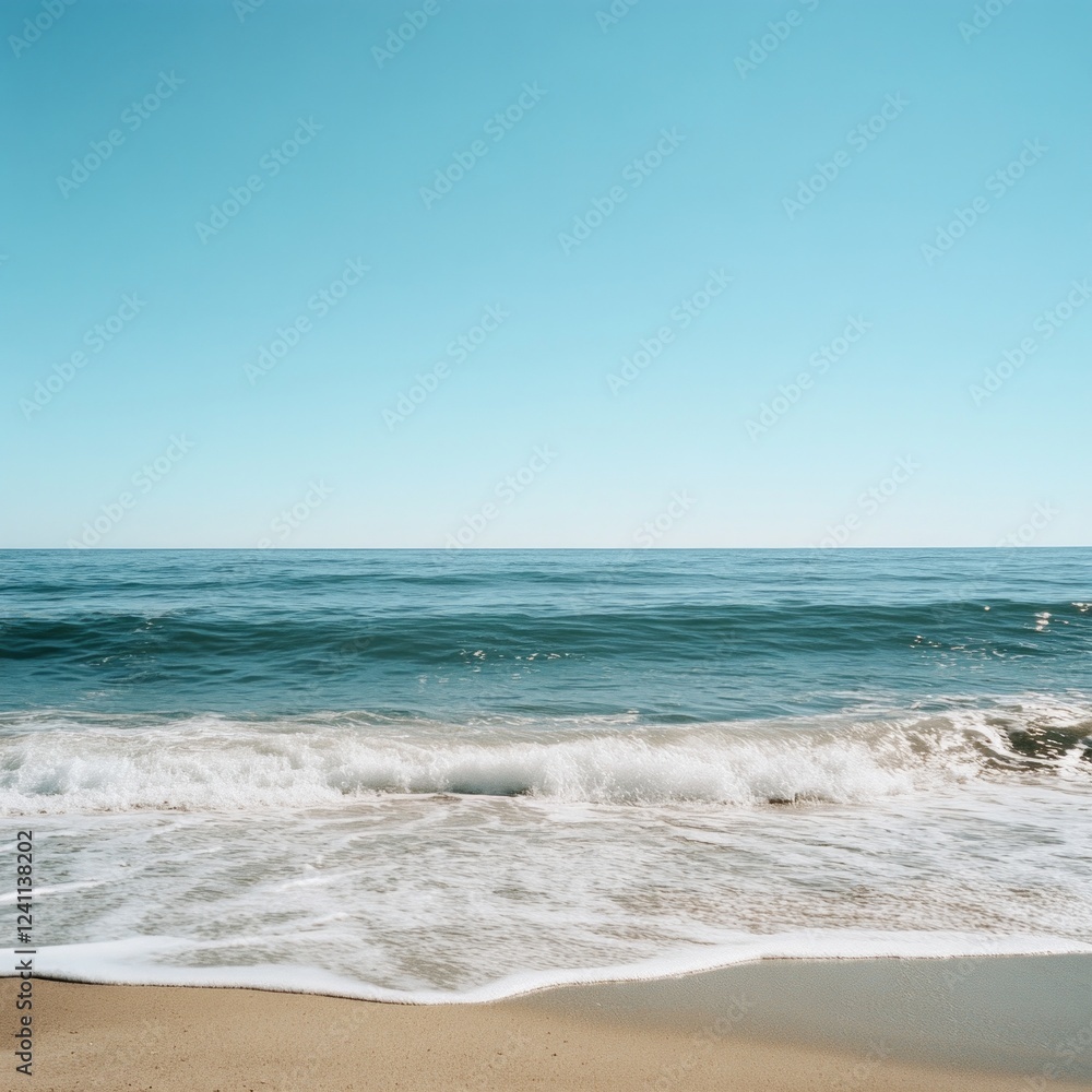 Tranquil ocean waves gently crashing on sandy beach under clear blue sky Tranquil ocean waves gently crashing on sandy beach under clear blue sky