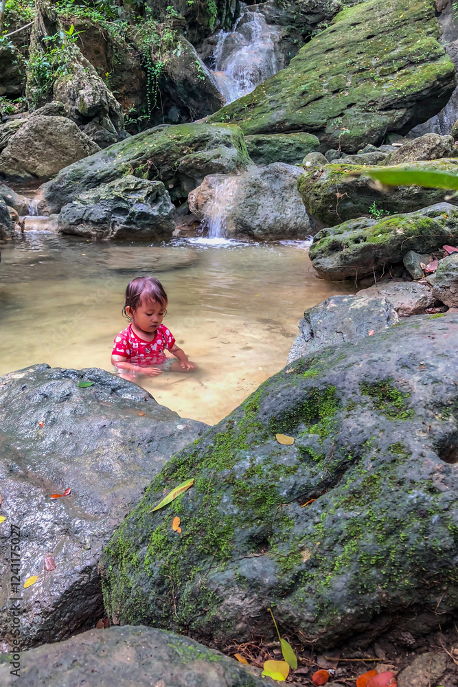 little asian girl playing by the waterfall with a heart full of laughter.