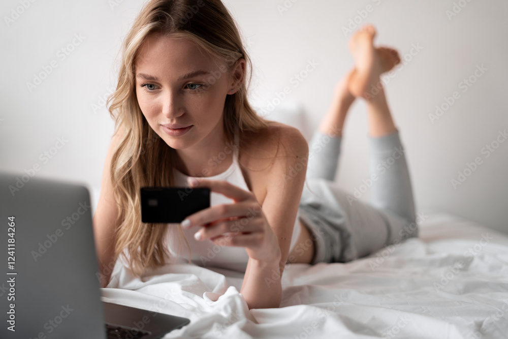 Cheerful woman shopping online at home, using credit card and laptop, lying on bed booking or ordering from internet Cheerful woman shopping online at home, using credit card and laptop, lying on bed booking or ordering from internet