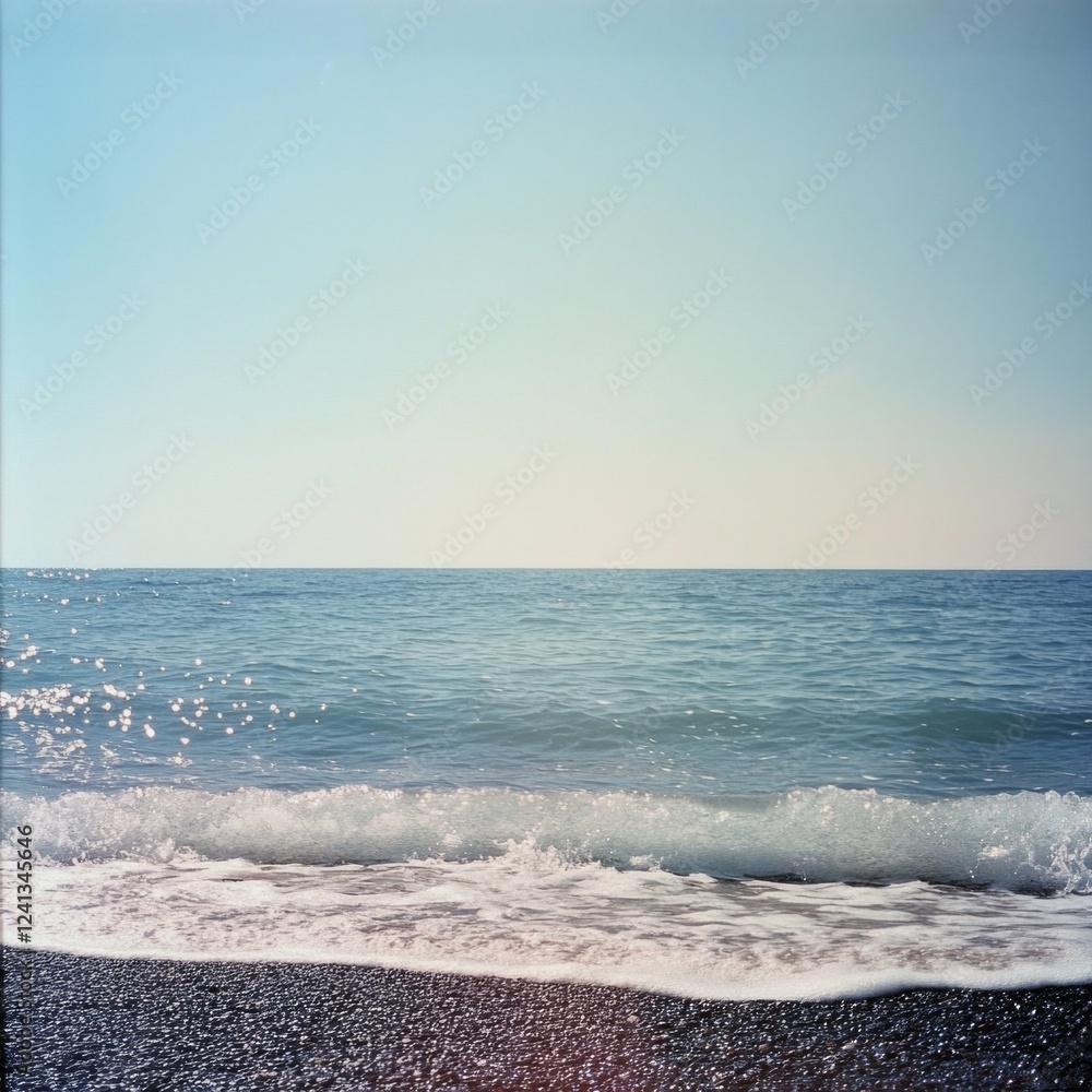 Fototapeta premium Tranquil ocean waves lapping against a pebble beach under a clear sky