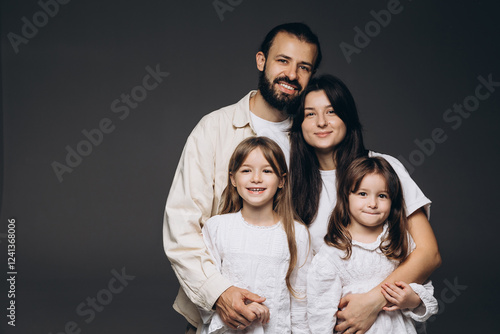 beautiful studio family portrait where the father hugs his wife and two little daughters