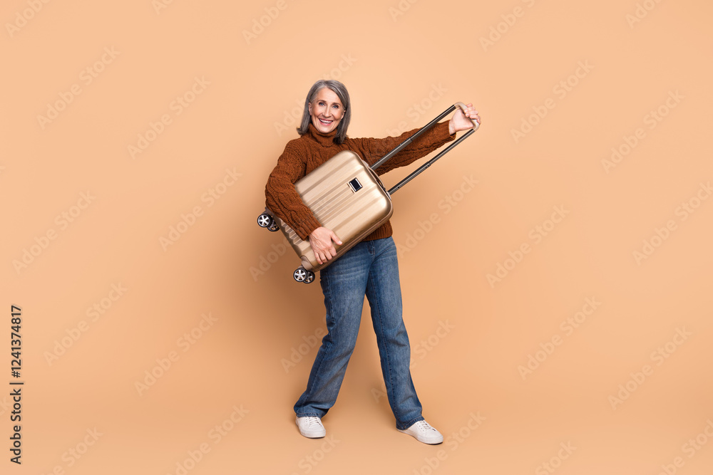 Smiling mature woman holding suitcase against beige background, enjoying travel and expressing happiness Smiling mature woman holding suitcase against beige background, enjoying travel and expressing happiness