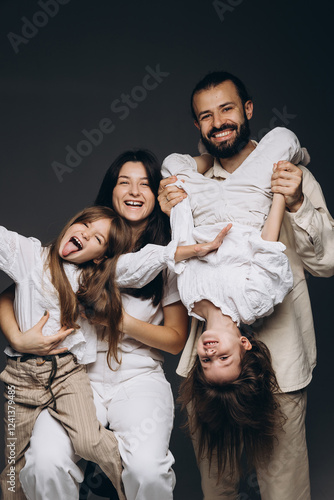 A young sincere family where a stylish bearded father and a cute wife hold their cute children in their arms. Family photo shoot in the studio