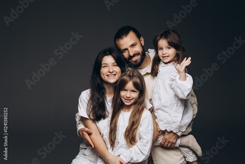A young sincere family where a stylish bearded father and a cute wife hold their cute children in their arms. Family photo shoot in the studio