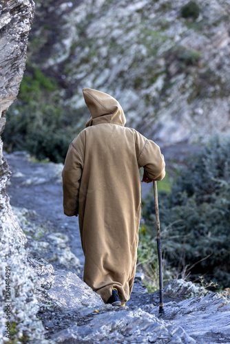 Man wearing a traditional Berber coat walking on a mountain path in Azrou, Morocco photo