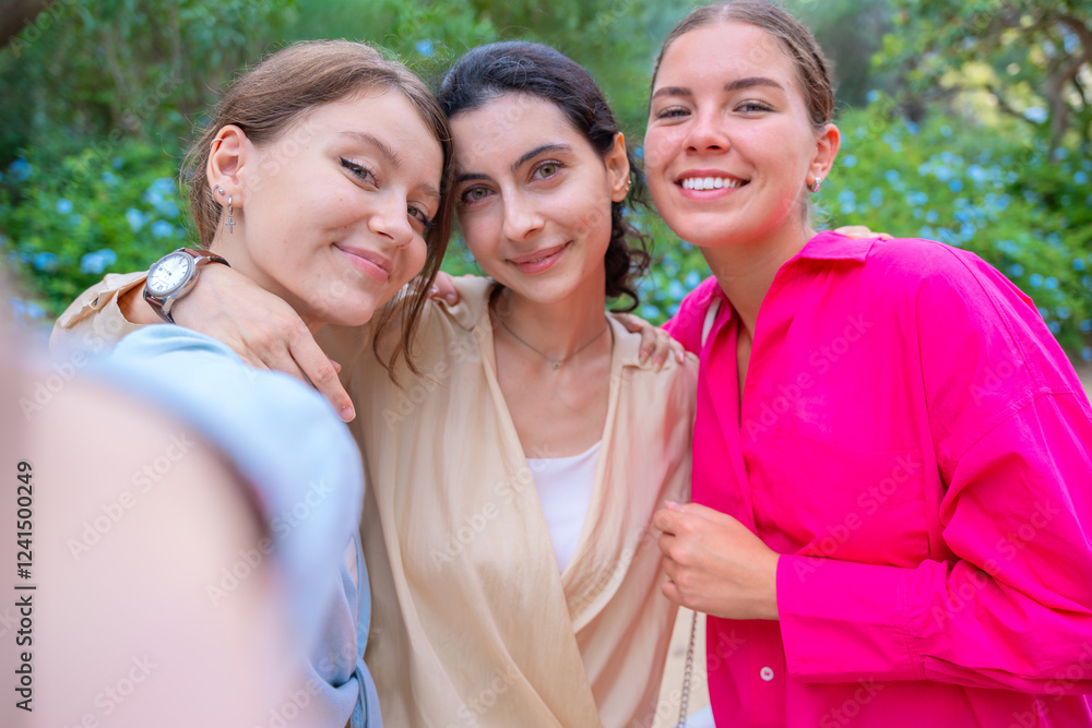 Three smiling women posing for a selfie in a lush green park. They embrace each other, expressing happiness and friendship. The vibrant colors and natural background create a joyful atmosphere. Three smiling women posing for a selfie in a lush green park. They embrace each other, expressing happiness and friendship. The vibrant colors and natural background create a joyful atmosphere.