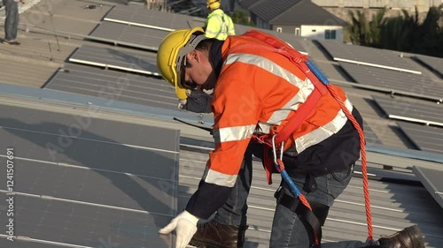 A technician inspects and repairs solar panels on a rooftop installation. The worker wears protective gear and focuses on ensuring the system is functioning well. The sky is clear and bright.