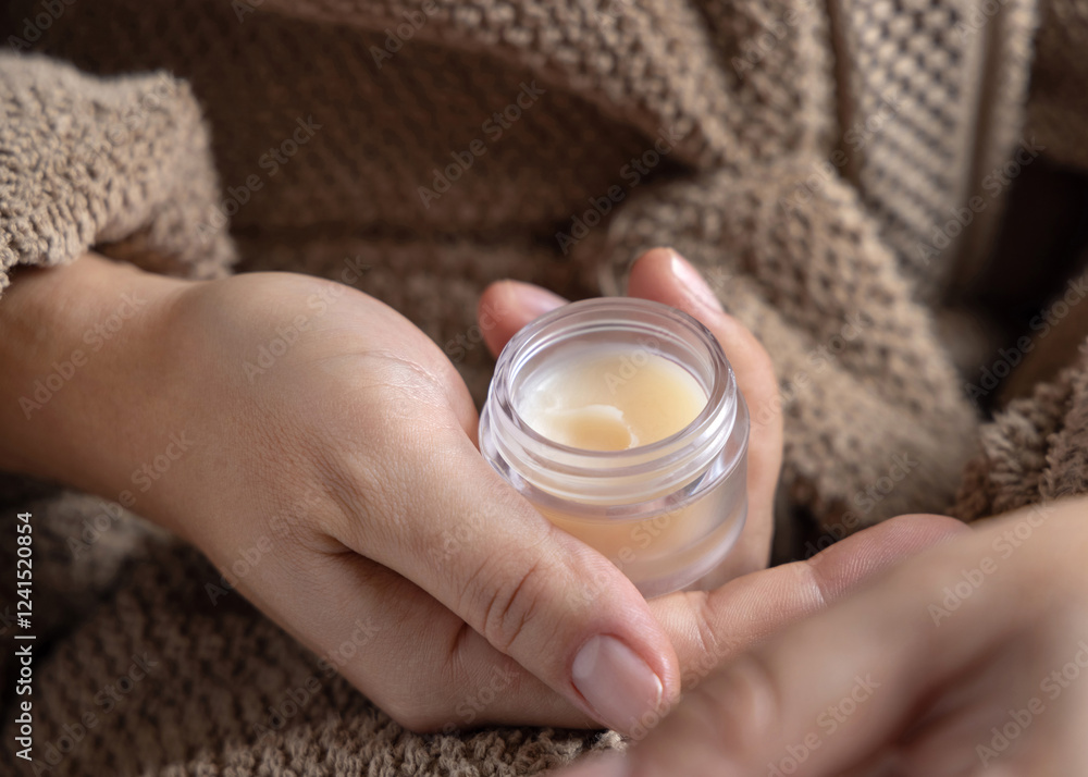 Closeup of woman in brown bathrobe holding opened lip balm jar in hands, cosmetic mockup Closeup of woman in brown bathrobe holding opened lip balm jar in hands, cosmetic mockup