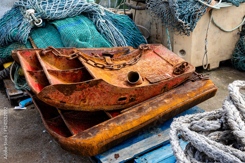 collection of weathered fishing equipment, trawl doors, nets and rope, situated on pallets on the concrete dockside