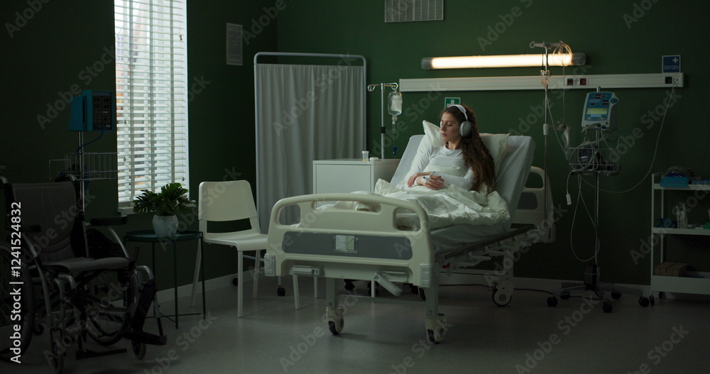 Young woman lies in a hospital bed, wearing headphones. Young woman lies in a hospital bed, wearing headphones.