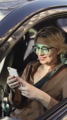 Mature woman sitting in car and chatting with friends on smartphone, dating app
