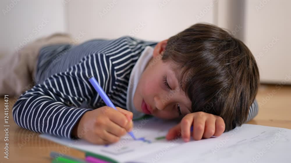 Young boy lying on floor, resting head on arm while drawing with blue pencil, immersed in creativity, expressing concentration, relaxation, and artistic engagement Young boy lying on floor, resting head on arm while drawing with blue pencil, immersed in creativity, expressing concentration, relaxation, and artistic engagement