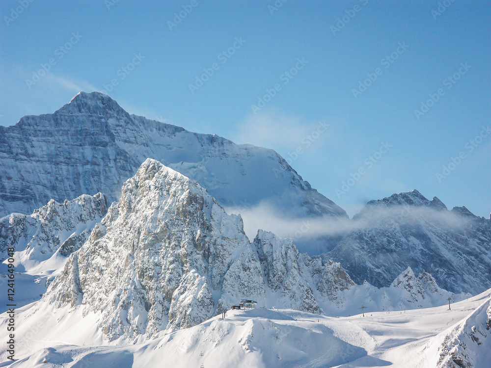 Fototapeta premium A snowy rocky mountain range and blue sky with a forest near a ski resort in the French or Swiss Alps in the winter