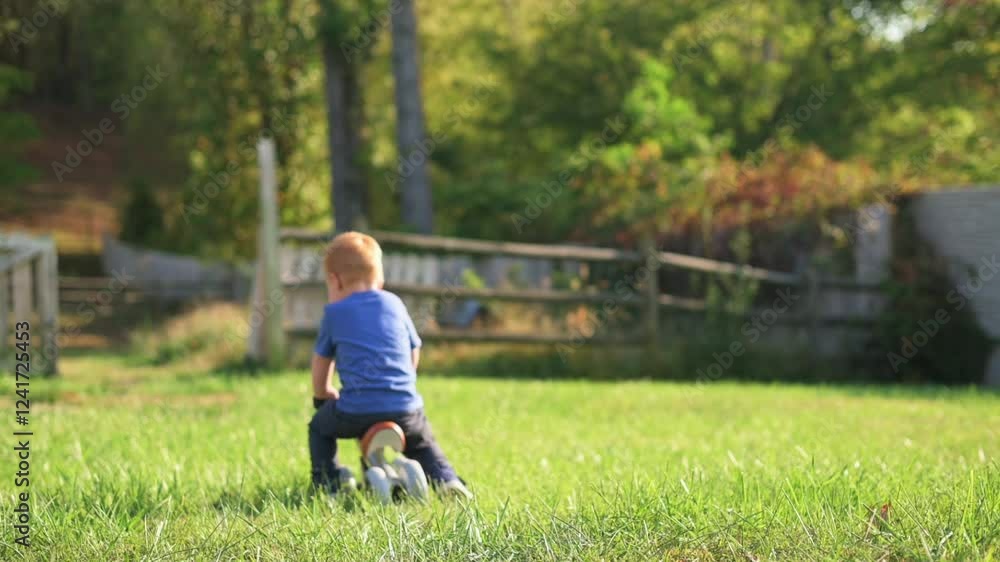 Toddler Playing Outdoors on Sunny Day. young child enjoys playing outside on toy in grassy yard surrounded by nature and wooden fence, basking in warm sunlight Toddler Playing Outdoors on Sunny Day. young child enjoys playing outside on toy in grassy yard surrounded by nature and wooden fence, basking in warm sunlight
