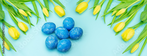 Frame of fresh cut yellow tulips and painted Easter eggs on a blue background. Spring Festival.