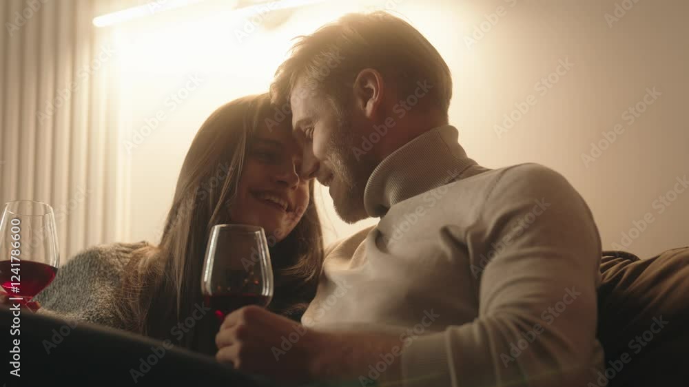 Couple enjoys red wine on sofa, laughing and talking. Couple enjoys red wine on sofa, laughing and talking.
