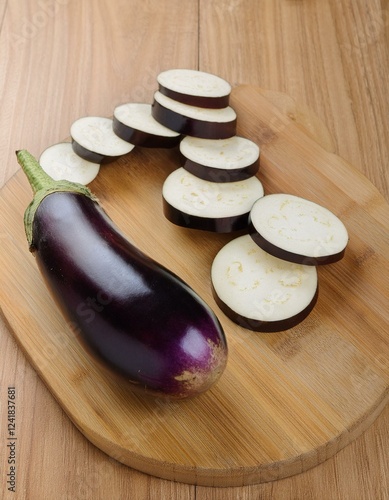 A vibrant purple eggplant sits beside its sliced counterparts on a light wood cutting board. photo