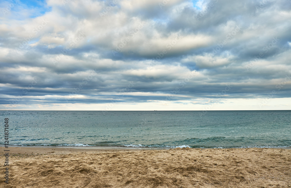 A tranquil sandy beach with gentle ocean waves under a dramatic cloudy sky.