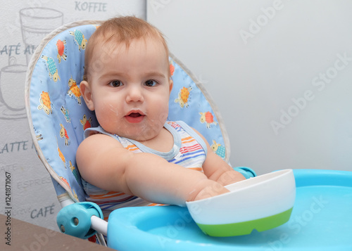 A cute baby sitting in a high chair with a colorful patterned cushion, playfully exploring their food. photo