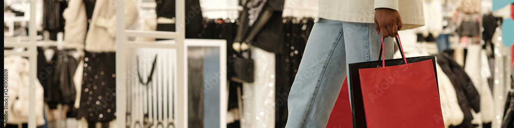 Obraz premium Header of hand and legs of young contemporary female consumer with shopping bags moving along large clothing store