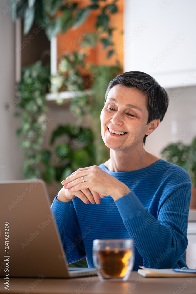 Content smiling mature woman with tea, make video call from laptop at home. Online virtual meeting, video conference, talk to colleagues, remote work and flexible working hours for online teacher Content smiling mature woman with tea, make video call from laptop at home. Online virtual meeting, video conference, talk to colleagues, remote work and flexible working hours for online teacher