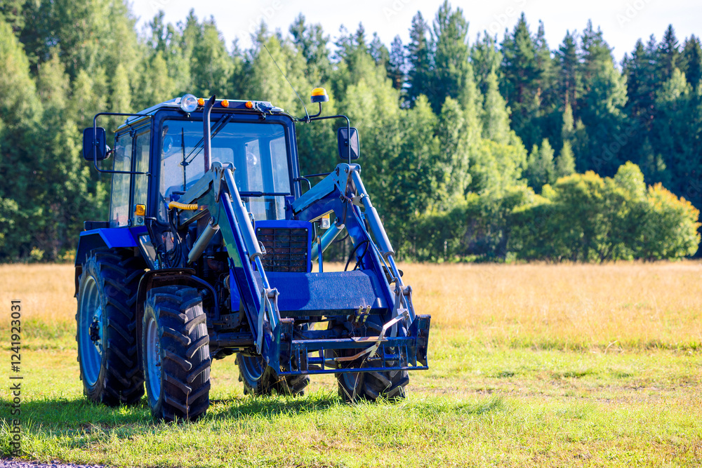 Fototapeta premium Blue tractor mowing grass in field on summer sunny day. High quality photo