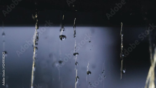 4K video of rain falling at night, illuminated by backlight. Raindrops visible against the dark background with audible rain sounds and occasional lightning strikes.