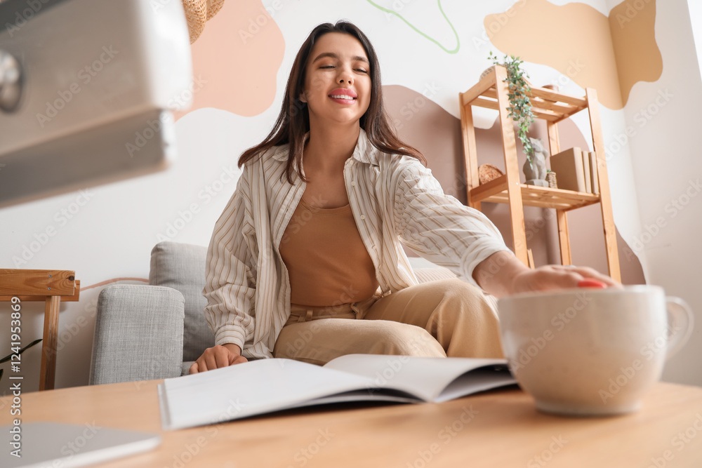 Young woman with magazine taking cup of coffee from table at home Young woman with magazine taking cup of coffee from table at home