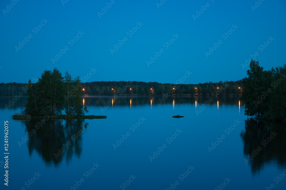 Fototapeta premium Early summer night by a calm lake in Finland with street lights lining the shore