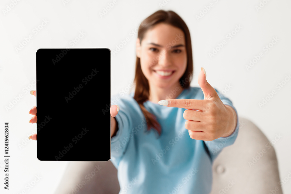 Joyful millennial woman pointing at tablet with blank screen for mockup, promoting new app, offering space for website or advertisement, selective focus. Touch pad display template Joyful millennial woman pointing at tablet with blank screen for mockup, promoting new app, offering space for website or advertisement, selective focus. Touch pad display template