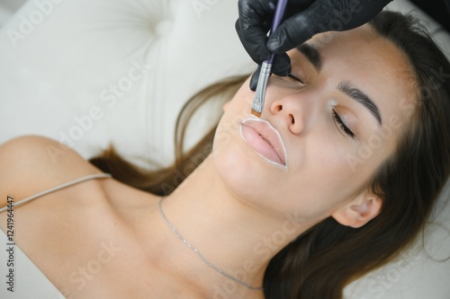 Woman beautician prepares the patient, a young woman, for permanent makeup lips, drawing the boundaries of a pencil in the office photo