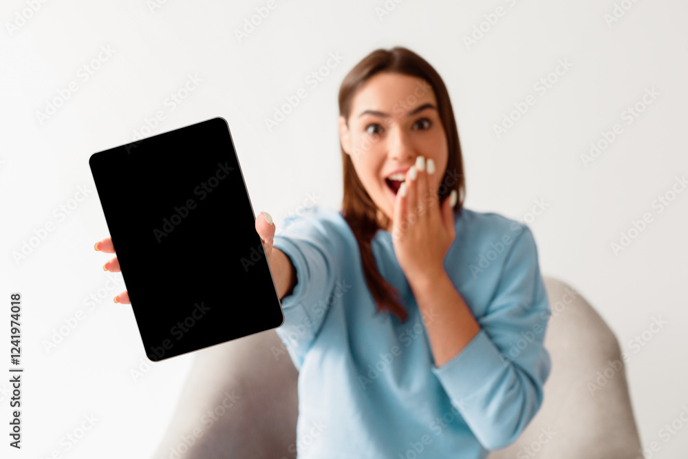 Shocked young woman showing tablet computer with black blank screen for mockup, covering mouth in surprise, advertising new app, offering empty space for website, white background. Selective focus Shocked young woman showing tablet computer with black blank screen for mockup, covering mouth in surprise, advertising new app, offering empty space for website, white background. Selective focus