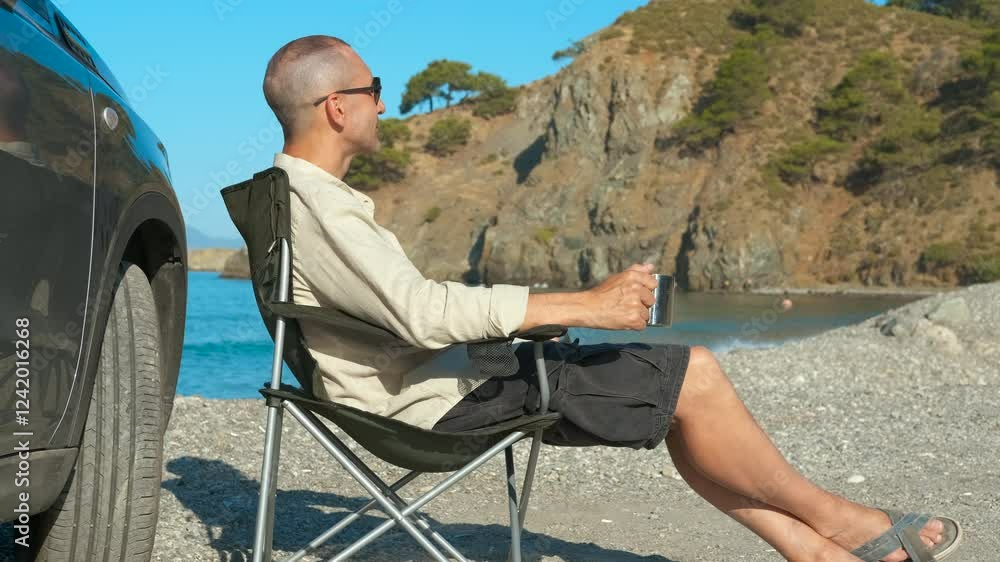 Tourist relaxing drinking coffee on beach. Man is enjoying a sunny day at the beach, sitting in a folding chair next to his car, drinking coffee and admiring the view Tourist relaxing drinking coffee on beach. Man is enjoying a sunny day at the beach, sitting in a folding chair next to his car, drinking coffee and admiring the view