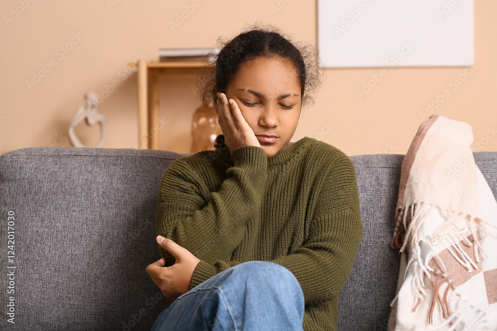 Cute African-American girl suffering from tooth ache and sitting on sofa at home Cute African-American girl suffering from tooth ache and sitting on sofa at home