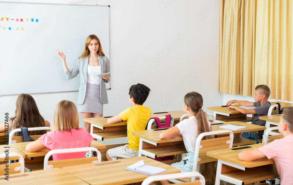 Young smiling woman teacher explaining new theme to children during class in primary school Young smiling woman teacher explaining new theme to children during class in primary school