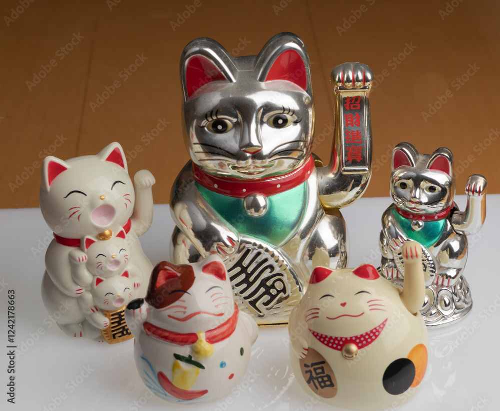 Grupo de figuras de gatos maneki-neko para la buena fortuna según la cultura japonesa, sobre una plataforma blanca Grupo de figuras de gatos maneki-neko para la buena fortuna según la cultura japonesa, sobre una plataforma blanca