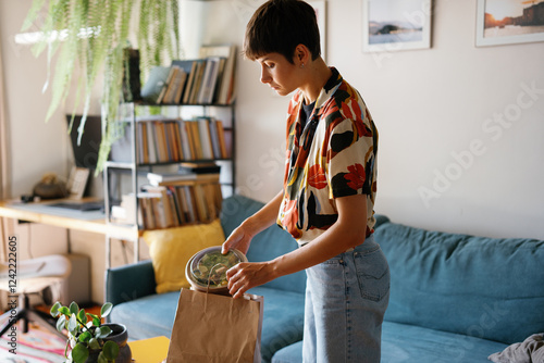 Woman taking bowl with takeout salad from package at home at daytime photo